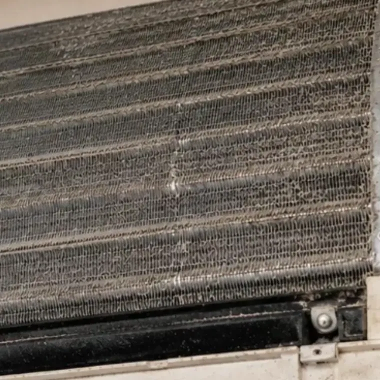 The coil of a wall mounted mini split, its fins packed grey with years of dust